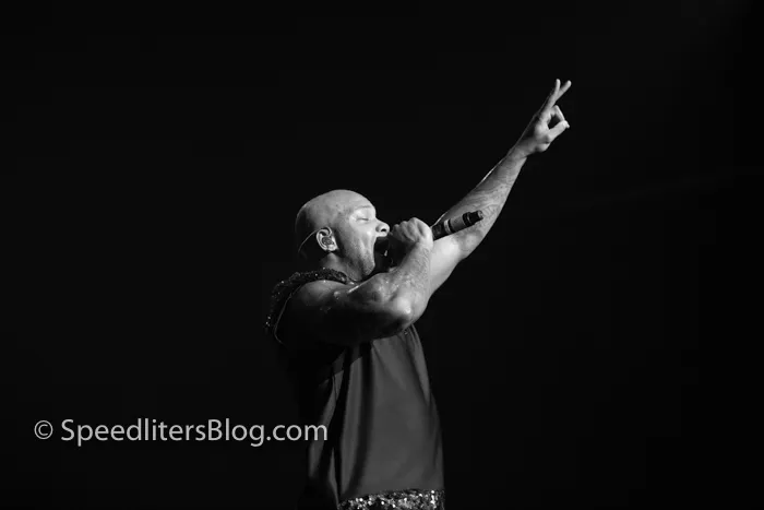 Flo Rida pointing up with a microphone in hand under a single stage spotlight, black and white