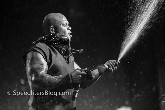 Flo Rida spraying a bottle of champagne on stage, black and white