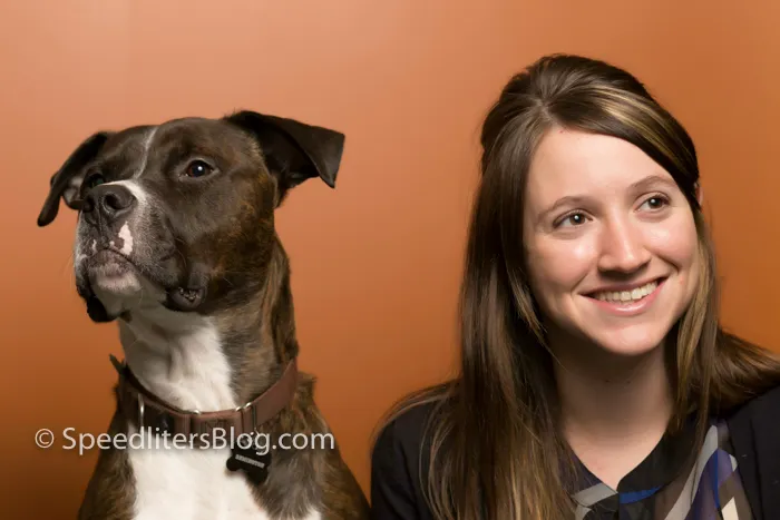 Brindle pit bull and smiling woman posed together in front of an orange backdrop