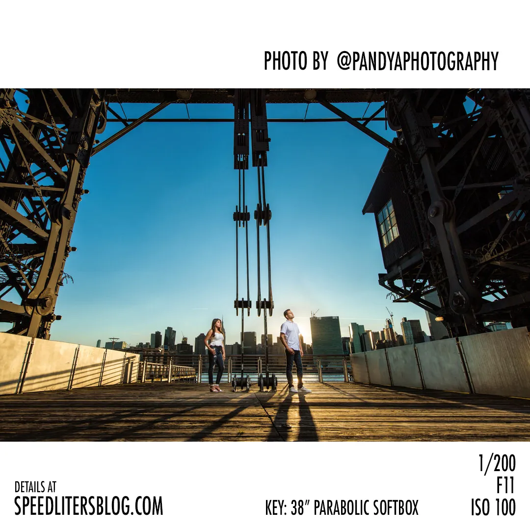 Couple standing apart under an industrial gantry on a New York waterfront at sunset, lit by a softbox, photo by Pandya Photography