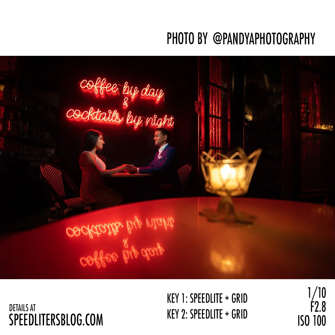 Couple holding hands at a restaurant table beneath a red neon sign, lit by two gridded speedlites, photo by Pandya Photography