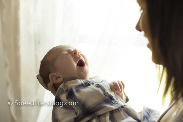 Newborn yawning in her mother’s arms in soft window light