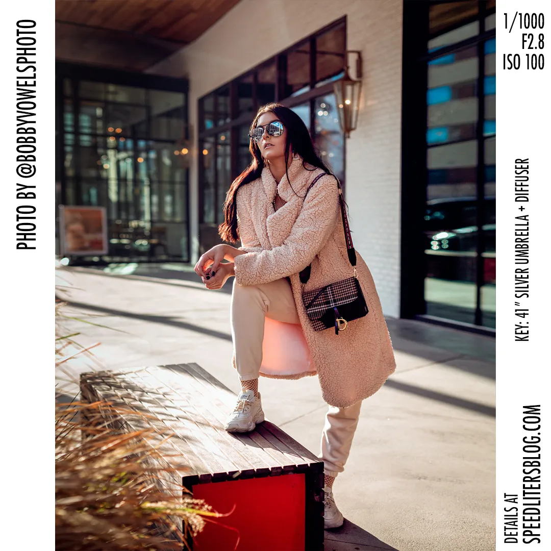Woman in a teddy coat and sunglasses posing by a storefront in bright sun, by Bobby Vowels