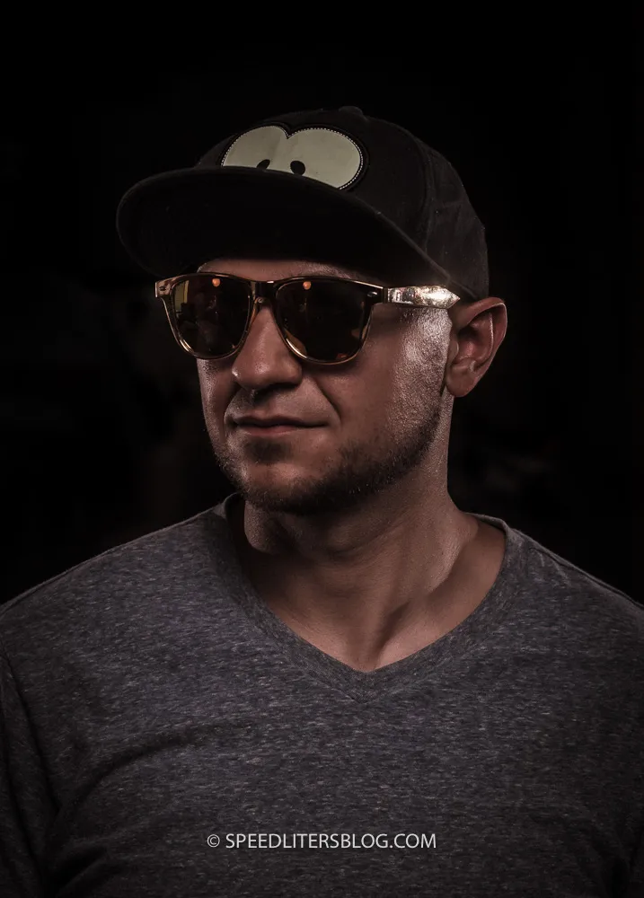 Man in a cap and sunglasses lit by hard side light from bare speedlites