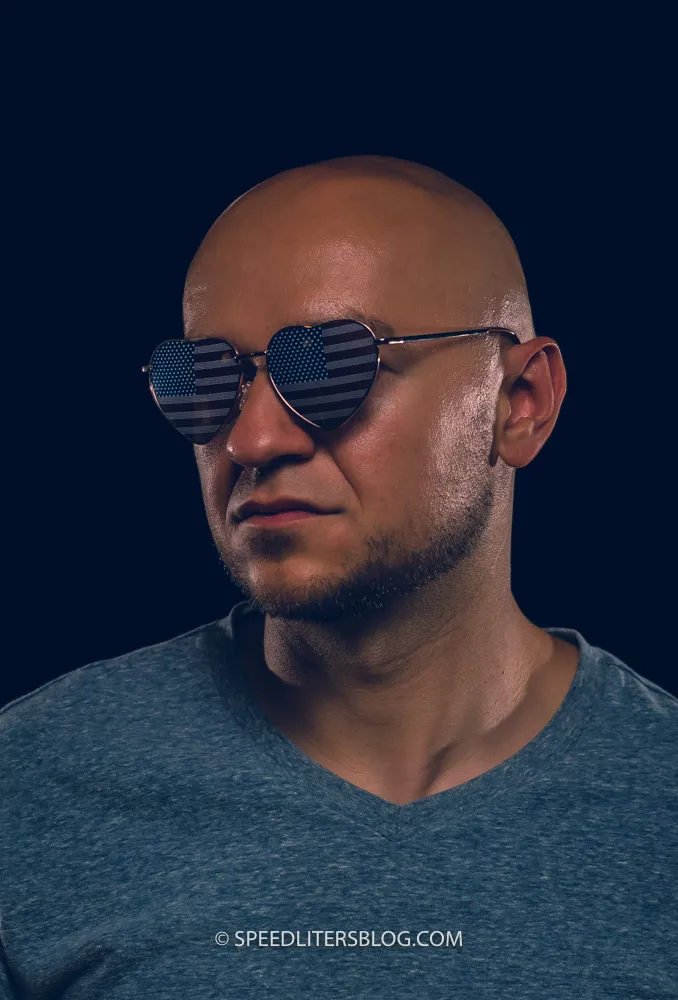 Man in heart-shaped flag sunglasses against a navy background, three-speedlite portrait