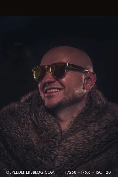 Man in a fur coat and sunglasses laughing, dramatic three-speedlite portrait