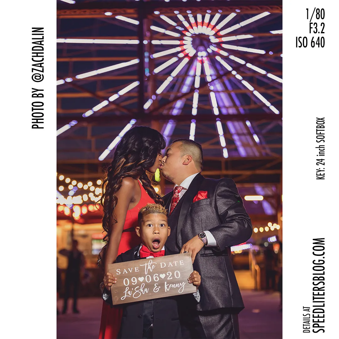Couple kissing by a Ferris wheel while their son holds a save-the-date sign, by Zach Dalin