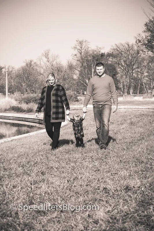 Black-and-white photo of parents walking hand in hand with their toddler in a park