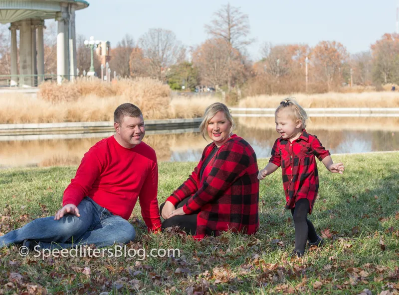 Family in red plaid playing on the grass beside a pond in fall