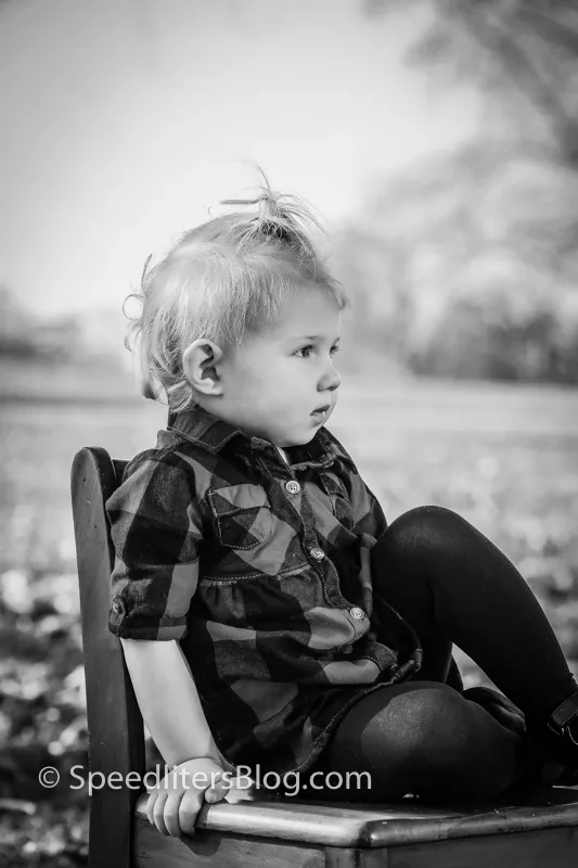 Black-and-white photo of a toddler in plaid sitting on an old wooden chair outdoors