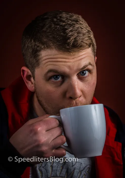 Man sipping from a white mug, colorful headshot against a red wall