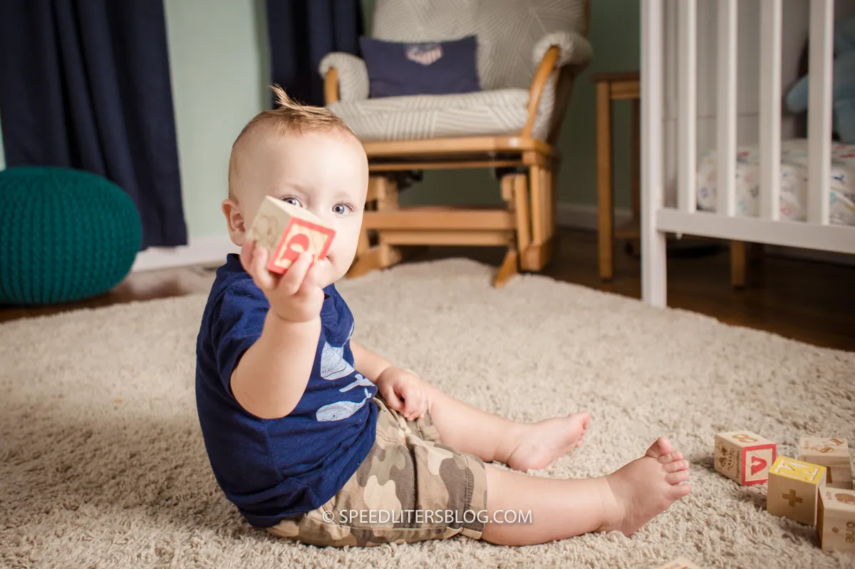 One-year-old holding up a wooden block in his nursery
