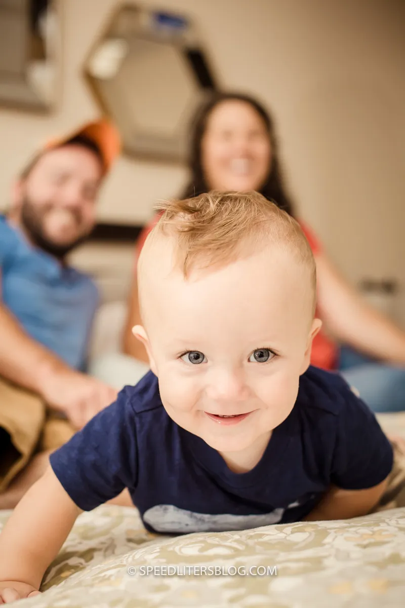 One-year-old crawling toward the camera with his parents smiling behind him