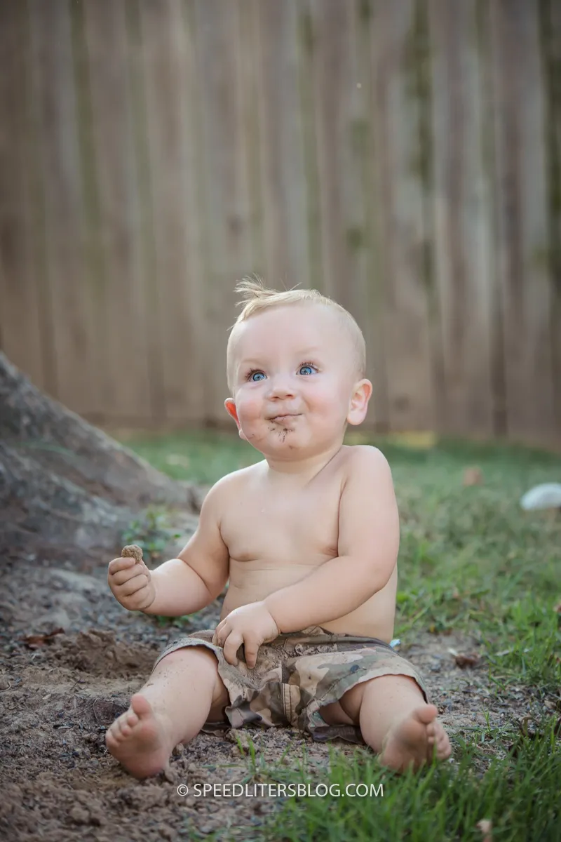 Toddler sitting in the dirt with a muddy face, grinning