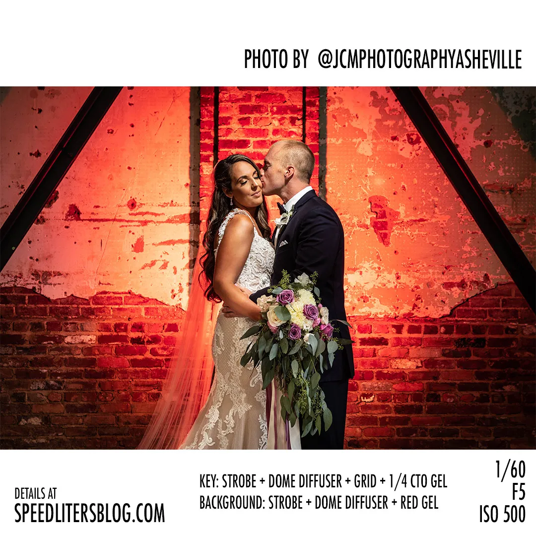 Groom kissing the bride against a red-lit brick wall, by JCM Photography