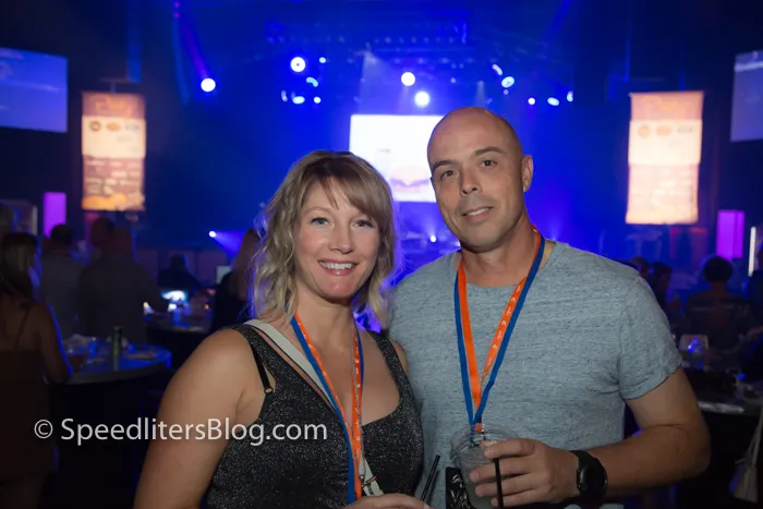 Couple at a nightclub event with blue stage lights behind them, lit by on-camera flash