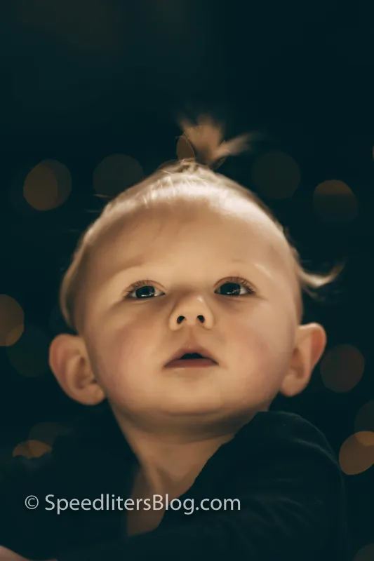 Close-up of a baby looking up with bokeh lights behind her