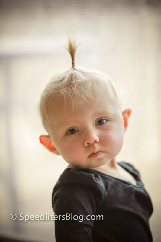 Close-up of a one-year-old with a wispy topknot in soft window light