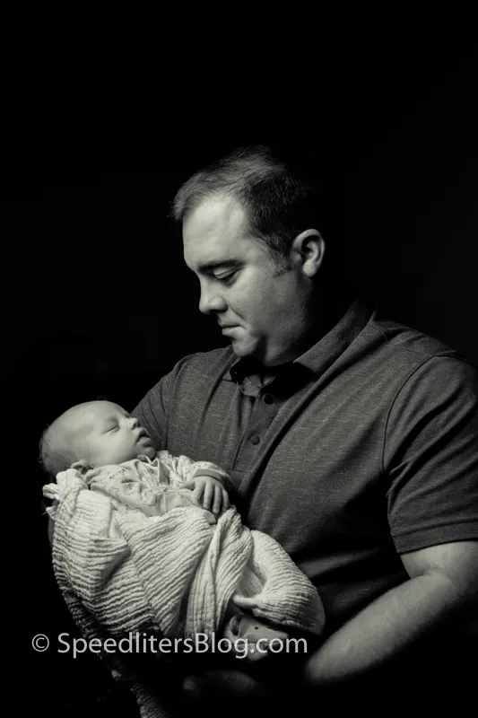 Black-and-white photo of a father cradling his newborn, lit by a single softbox