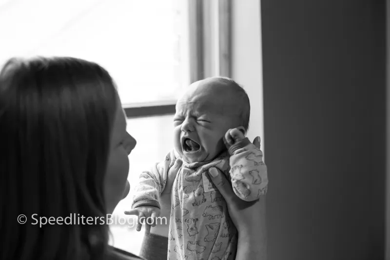 Black-and-white photo of a mother holding up her crying newborn by a window