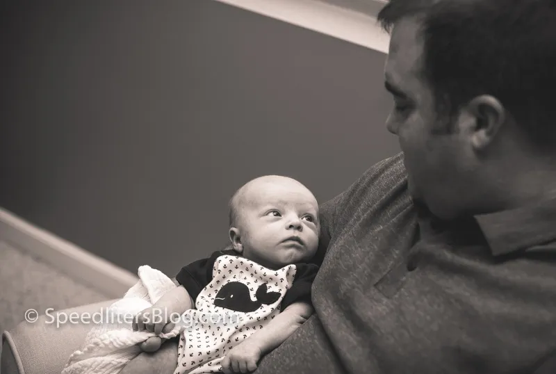 Father holding his newborn son, who looks up at the camera