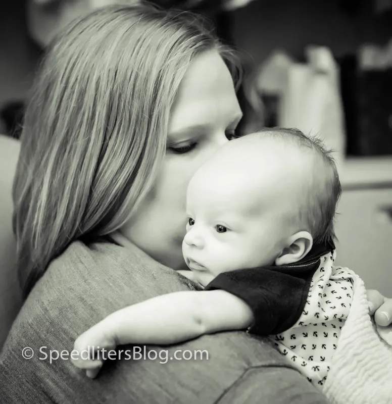 Black-and-white photo of a mother kissing the head of the baby on her shoulder