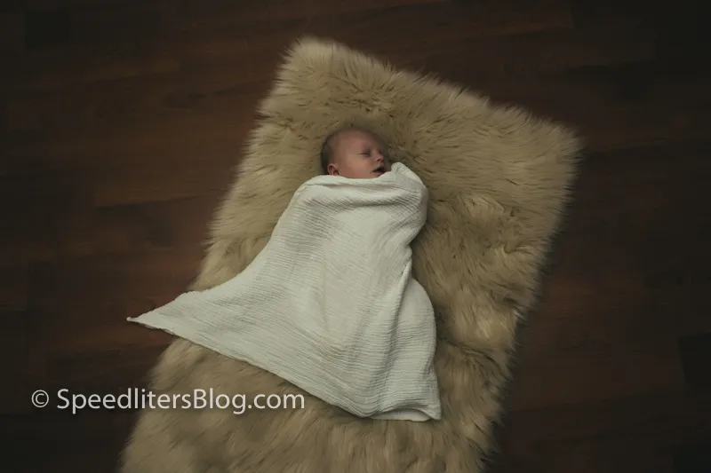 Newborn swaddled on a fur rug on a wood floor, shot from above