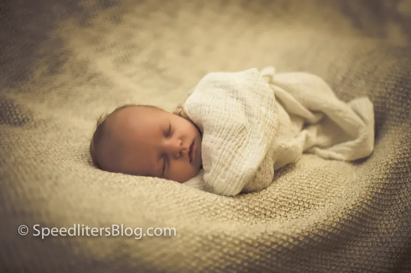 Sleeping newborn wrapped in a muslin blanket on a knit throw