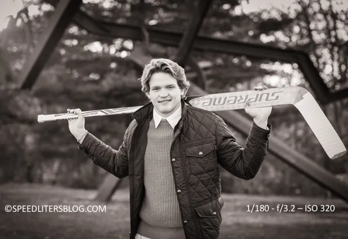 Black-and-white photo of a senior holding a hockey stick across his shoulders