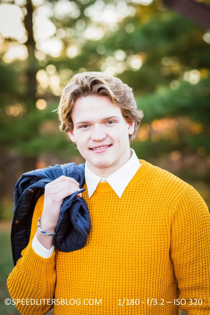 Senior in a mustard sweater with a jacket over his shoulder, smiling outdoors
