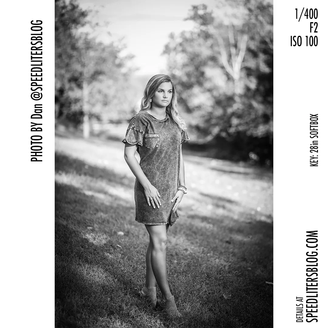 Black-and-white photo of a senior girl in a T-shirt dress standing in a field
