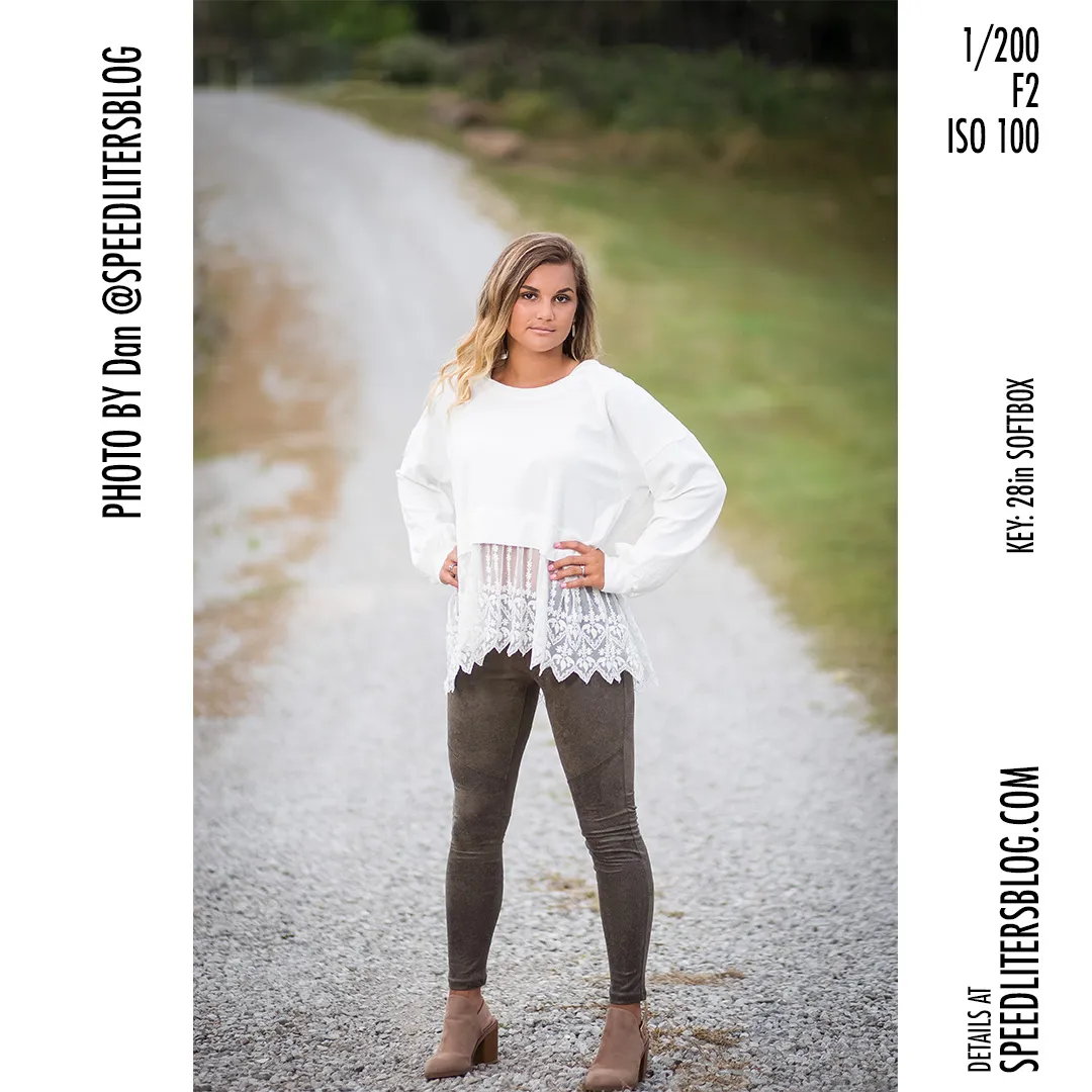 Senior girl in a white lace top standing on a gravel road