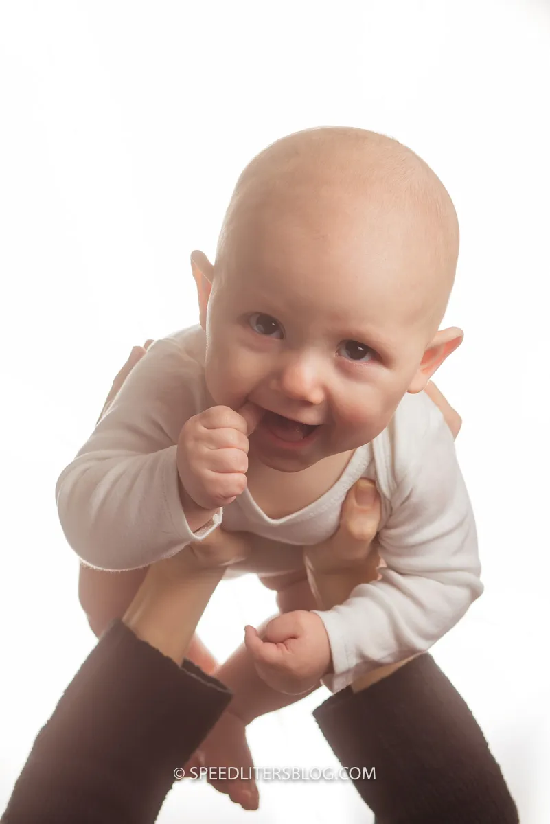 Smiling five-month-old held up by his parent against a white background