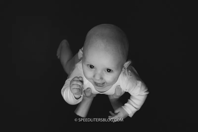 Black-and-white photo of a baby held up against a dark red wall