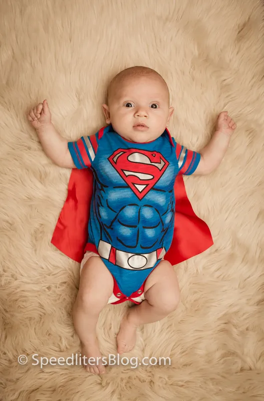 Baby in a Superman outfit and cape lying on a fur rug, lit by bounce flash